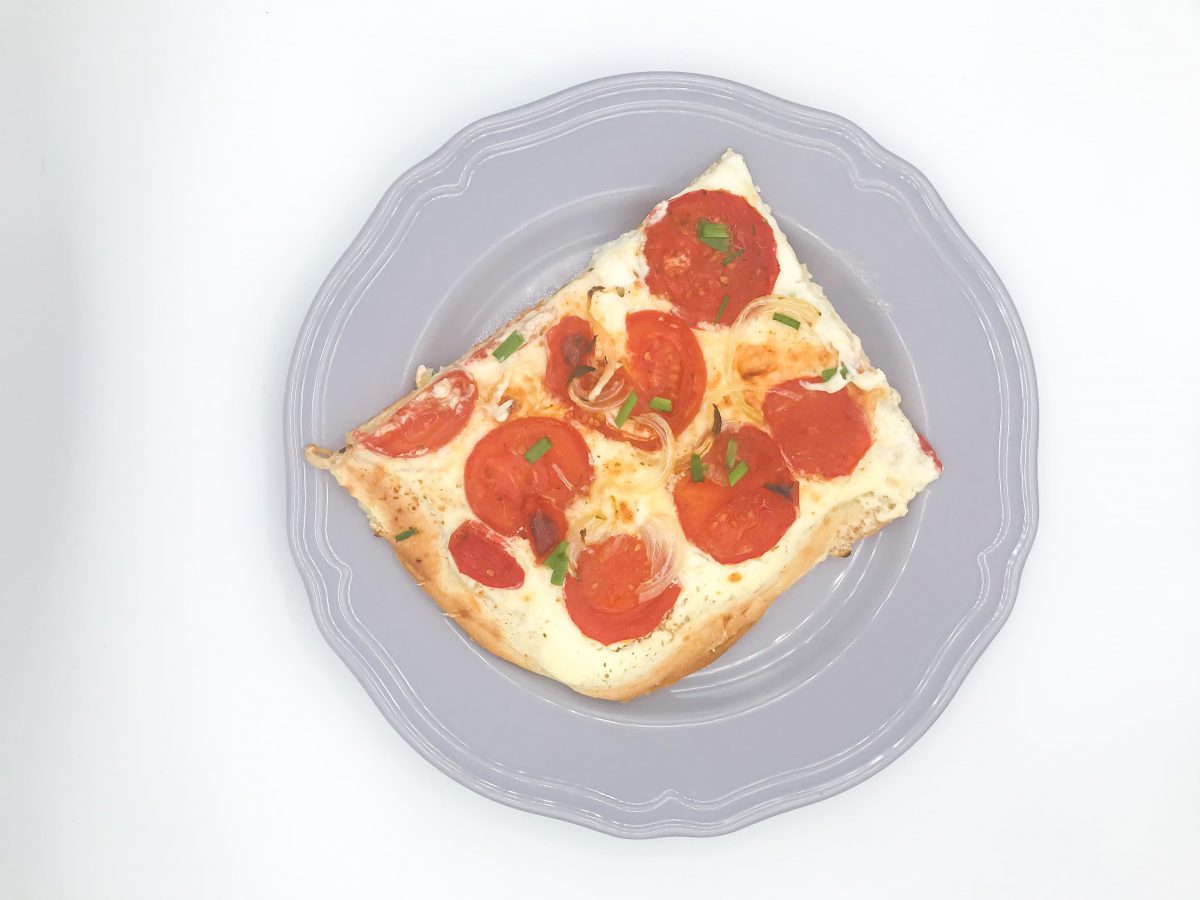 Von oben fotografiert: Ein Teller, darauf ein Stück Tomatenpizza.